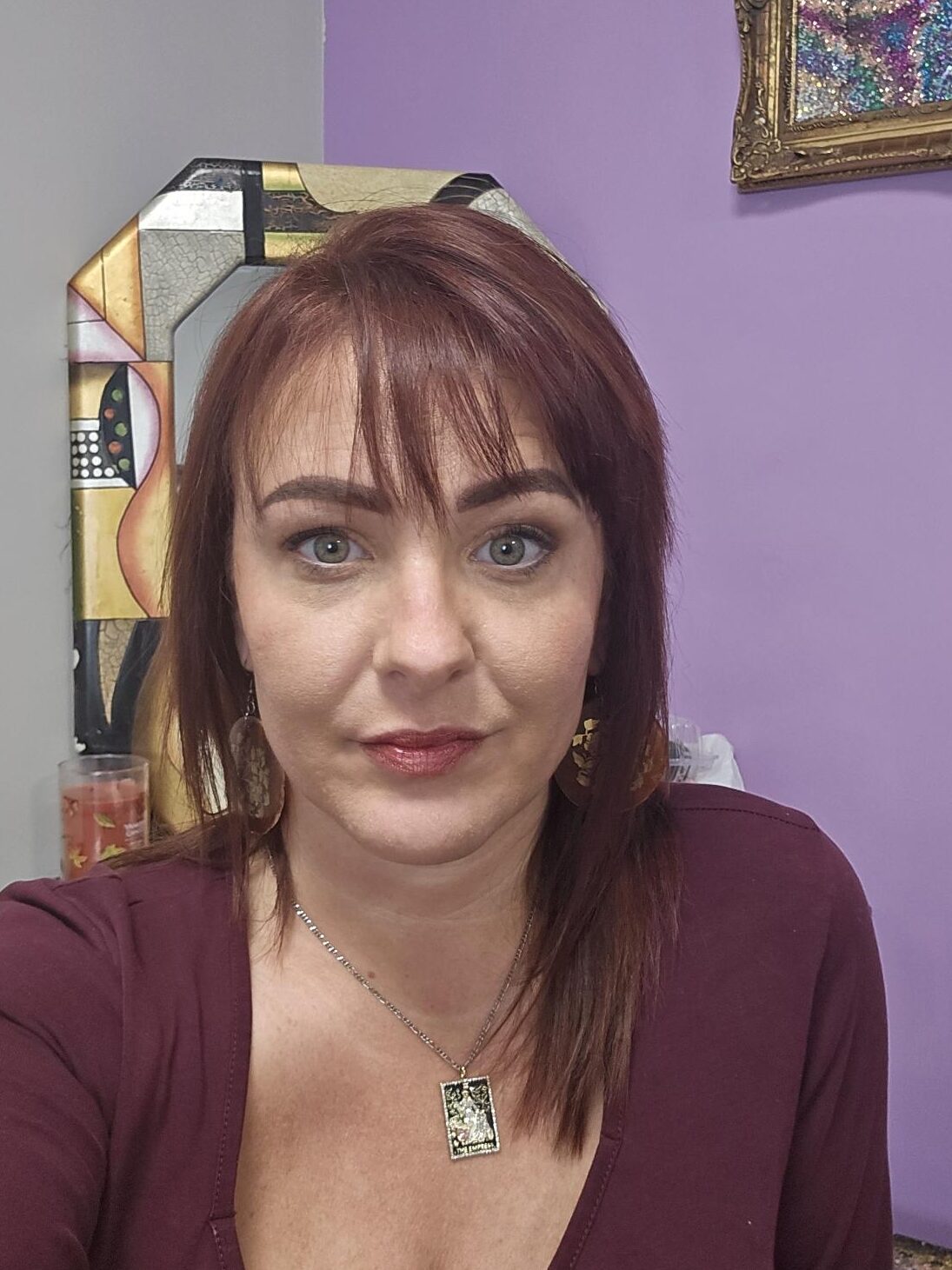Woman with auburn hair and a pendant necklace against a purple background.